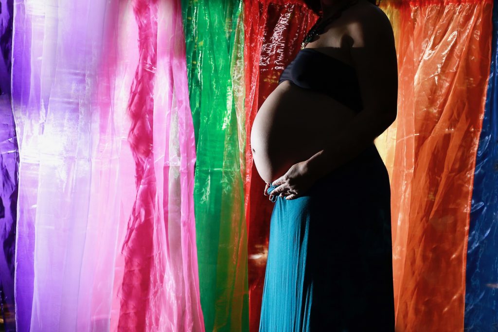Pregnant woman in front of rainbow curtain. You don't move on from a loss, even with a rainbow baby.